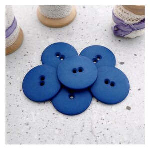May include: A collection of six circular, deep blue buttons arranged in a cluster. Each button features a smooth, matte finish and two central holes for attachment. The buttons are positioned together, showcasing their uniform color and shape.