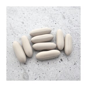 May include: A collection of beige, oblong-shaped capsules. The capsules are arranged in a close-up shot, with some overlapping. The background is a light gray, textured surface. The capsules appear to be a dietary supplement or medication.