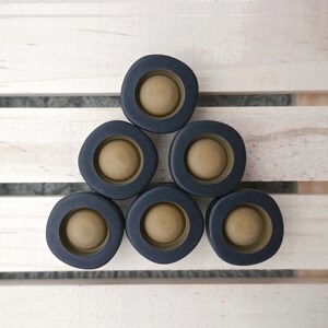 May include: A set of six circular buttons arranged in a pyramid formation. Each button features a matte black outer ring surrounding a smooth, light tan, convex center dome. The buttons have a uniform, rounded square shape with smooth edges.