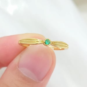 Op de afbeelding: Een gouden ring met een groene edelsteen in het midden. De ring heeft een delicaat, gebogen ontwerp.