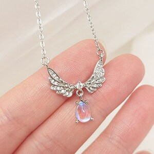May include: Silver necklace with a teardrop-shaped iridescent gemstone pendant and angel wings with clear crystal accents.