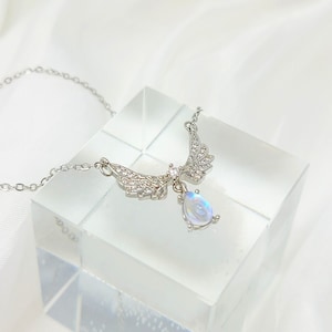 May include: A silver necklace with a teardrop-shaped moonstone pendant and a pair of angel wings adorned with clear cubic zirconia stones.