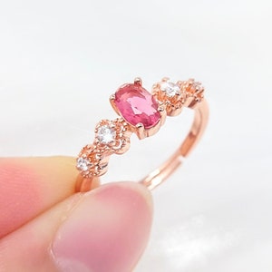 May include: Rose gold ring with an oval pink gemstone centre and smaller white gemstones. The ring has a delicate, floral design, ideal for adding a touch of elegance to any outfit.