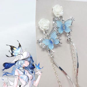 May include: A pair of silver-toned dangle earrings featuring white rose studs, light blue butterfly charms with small clear crystals, and long, thin silver chains that hang down from the butterfly motifs, creating a delicate and layered appearance.