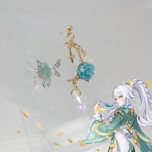 May include: Earrings with a gold crescent moon design, a blue rose, and a clear crystal drop. Another earring features a butterfly wing design with iridescent details. The earrings are displayed on a clear surface.
