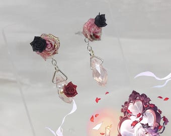 Könnte beinhalten: Ohrringe mit rosa und schwarzen Rosenakzenten. Jeder Ohrring hat einen kleinen Rosenstecker, einen hängenden Kristall und eine kleinere rote Rose. Die Ohrringe sind auf einer transparenten Oberfläche ausgestellt.