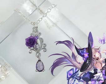 Könnte beinhalten: Eine silberfarbene Anhängerkette mit einer lila Rose und einem tropfenförmigen Amethysten. Der verzierte Anhänger hat ein filigranes Design mit kleinen lila Edelsteinen. Die Halskette wird auf einer klaren, reflektierenden Oberfläche präsentiert.