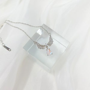 May include: A silver necklace with a teardrop-shaped iridescent stone pendant and a pair of angel wings with clear crystals.