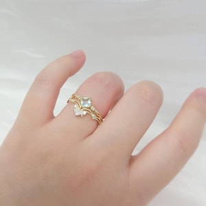 May include: A gold ring set featuring a square, light blue gemstone and a delicate, curved band. The ring is adorned with small, sparkling accent stones. The design is elegant and suitable for special occasions.