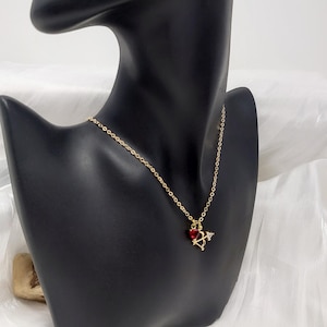K&ouml;nnte beinhalten: Eine goldene Kettenkette mit einem kleinen roten Herz-Anh&auml;nger mit einem goldenen Pfeil. Der Anh&auml;nger ist ein Symbol f&uuml;r Liebe und Romantik.