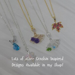 May include: A collection of silver and gold necklaces with various pendant designs. Pendants include a butterfly, a fan with purple roses, a fan with white and blue roses, a maple leaf, and a mermaid tail. Text on the image reads "Lots of other Genshin Inspired Designs Available in my Shop!"