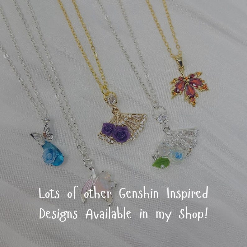 May include: A collection of silver and gold necklaces with various pendant designs. Pendants include a butterfly, a fan with purple roses, a fan with white and blue roses, a maple leaf, and a mermaid tail. Text on the image reads "Lots of other Genshin Inspired Designs Available in my Shop!"