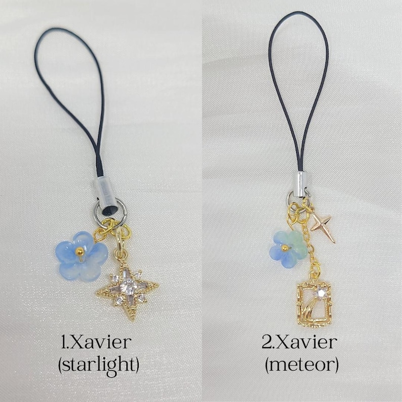 May include: Two phone charms with black loops and silver connectors. The first, 1.Xavier (starlight), features a blue flower and a gold star charm with clear crystals. The second, 2.Xavier (meteor), has a blue flower, a small gold cross, and a gold rectangular frame charm with a crystal.