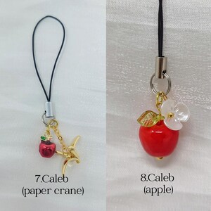 May include: Two phone charms with black cords. The first, labeled 7.Caleb, features a small red apple charm and a gold-toned metal paper crane. The second, labeled 8.Caleb, features a red apple charm with a green leaf and a white flower accent.