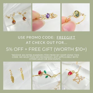 May include: A collage of gold-toned jewelry, including earrings with amber-colored teardrop pendants, rings with purple and green gemstones, a bracelet with a red rose, and a necklace with a heart and bow and arrow charm. Text reads: USE PROMO CODE: FREEGIFT.