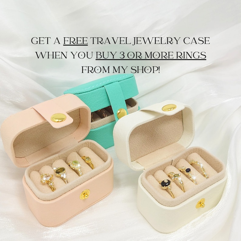 K&ouml;nnte beinhalten: Drei kleine Schmuckk&auml;stchen mit ge&ouml;ffneten Deckeln, die F&auml;cher f&uuml;r Ringe enth&uuml;llen. Die K&auml;stchen sind rosa, wei&szlig; und t&uuml;rkis. Der Text auf dem Bild lautet "GET A FREE TRAVEL JEWELRY CASE WHEN YOU BUY 3 OR MORE RINGS FROM MY SHOP!"