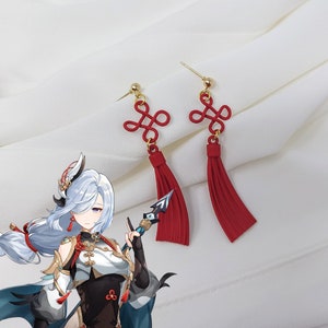 May include: A pair of red tassel earrings with a gold knot design. The earrings are made of a lightweight material and have a delicate, feminine look.