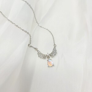 May include: A silver necklace with a teardrop-shaped iridescent stone pendant and a pair of wings with clear crystals.