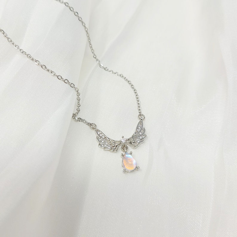 May include: A silver necklace with a teardrop-shaped iridescent stone pendant and a pair of wings with clear crystals.
