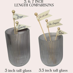 Puede incluir: Dos vasos de vidrio estriado, uno de 5 pulgadas y otro de 3,5 pulgadas de alto, que contienen palitos de madera rematados con peque&ntilde;as banderas de color crema. Las banderas tienen texto impreso como The Griggs, The Gutierrez, The Sengers, The Nolins y la fecha 04.25.26. La imagen incluye el texto 5, 6, 7 INCH LENGTH COMPARISONS.