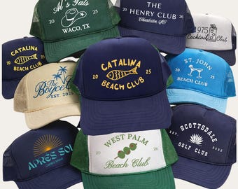 May include: A collection of trucker hats in various colors, featuring embroidered logos and text. Designs include "Al's Gals," "Catalina Beach Club," "The Henry Club," and "Scottsdale Golf Club." The hats have mesh backs and curved brims.