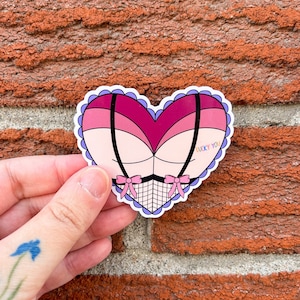 Puede incluir: Una pegatina en forma de corazón rosa y rojo con un diseño de encaje blanco y negro y el texto "Lucky You".