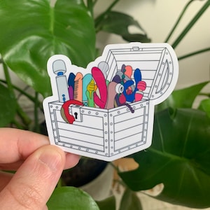 May include: A white sticker featuring a cartoon treasure chest overflowing with colorful, whimsical objects. The chest is open, revealing various shapes and sizes in shades of pink, blue, green, and purple. A red lock hangs on the front of the chest.