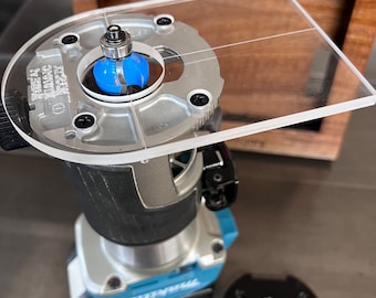 May include: A blue and black router with a clear plastic template attached to the top. The router has a black base and a blue handle. The template has a circle in the center and a grid pattern.