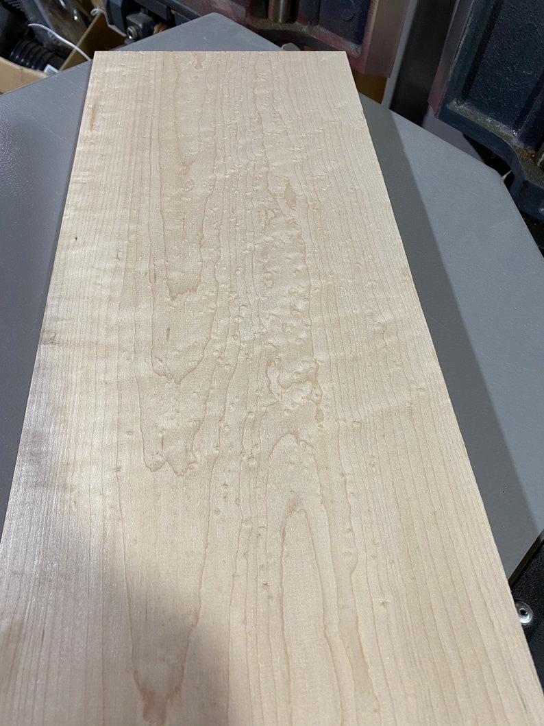 May include: A close-up of a light wood board with a natural wood grain pattern. The wood has a light brown color and a smooth surface.