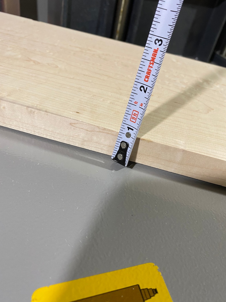 May include: A white tape measure with black markings is measuring a piece of light wood. The tape measure reads "CRAFTSMAN" and has markings for inches and feet.