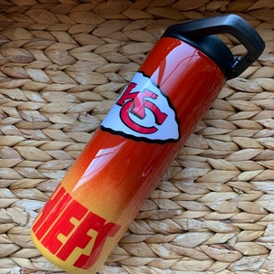 May include: A red and yellow stainless steel water bottle with a Kansas City Chiefs logo and the word "Chiefs" on the side. The bottle has a black lid with a carrying handle.