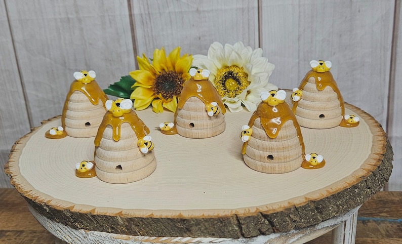 May include: Six wooden beehive-shaped ornaments with dripping honey and bee figurines. The ornaments are arranged on a wooden slice.