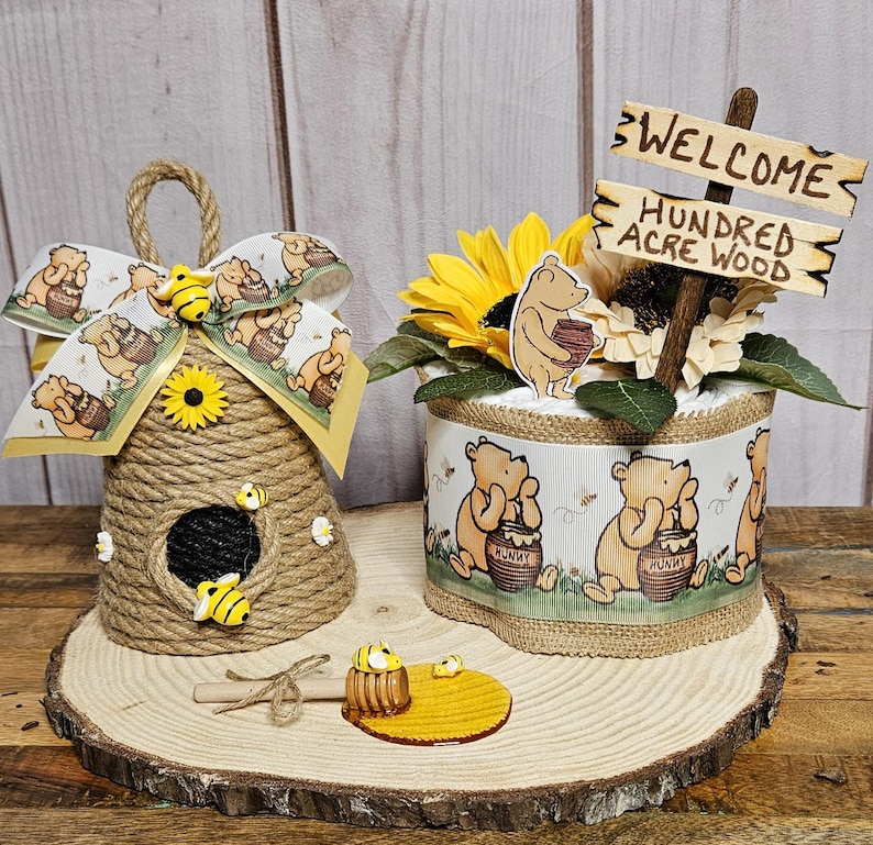 May include: A Winnie the Pooh themed baby shower centerpiece with a diaper cake decorated with Winnie the Pooh characters and a welcome sign that says "Welcome Hundred Acre Wood". The centerpiece also includes a handmade honey pot and a beehive.