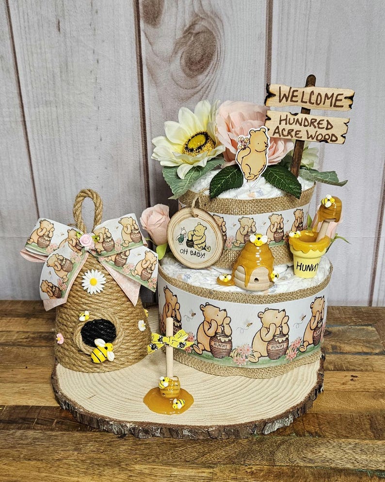 May include: A Winnie the Pooh themed diaper cake with a honey pot, bees, and a sign that says "Welcome to the Hundred Acre Wood".