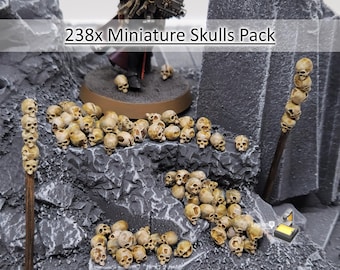May include: A 238x Miniature Skulls Pack featuring numerous small, beige, realistic-looking human skulls scattered across a dark gray rocky terrain, with some skulls stacked on wooden poles and others resting on the ground.