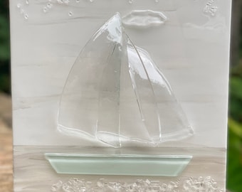 May include: A white canvas with a glass sailboat and a green glass boat on a white sandy beach with white glass dots representing the water.
