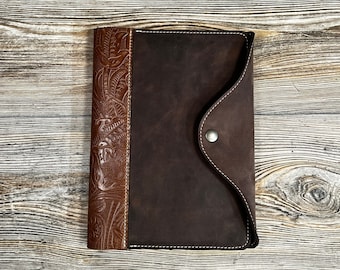 May include: A brown leather journal with a flap closure and a decorative embossed design on the front cover.