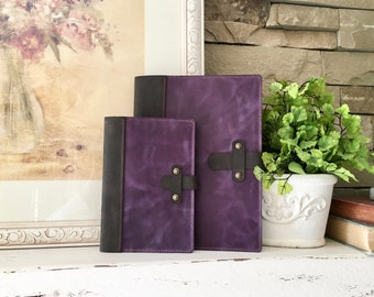 Könnte beinhalten: Zwei violette Lederjournale mit schwarzen Akzenten und Riemen. Die Journale liegen auf einer weißen Oberfläche.