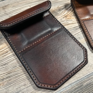 May include: Two brown leather wallets with stitched edges and a flap closure. The wallets have multiple compartments for cards and cash.