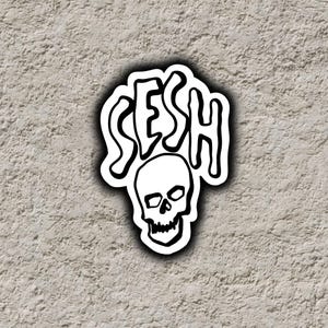 May include: A die-cut sticker featuring a black and white graphic design. The word SESH is written in a stylized, dripping font above a detailed illustration of a human skull. The entire design is outlined in white with a subtle drop shadow effect.