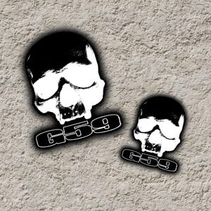 May include: Two black and white skull stickers. Each skull has a stylized design with the text "G59" below. The stickers are on a textured, light gray background.