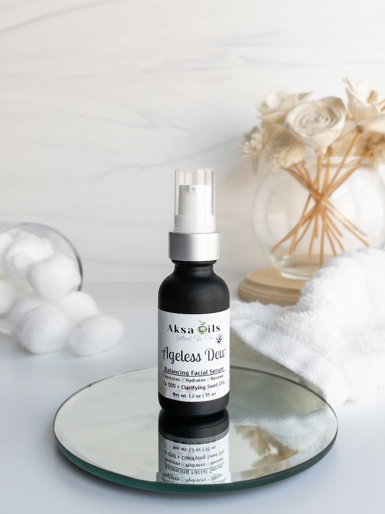 Może przedstawiać: Czarna szklana butelka z srebrną pompką i białą etykietą z napisem "Aksa Oils Natural Skin Care Ageless Dew Balancing Facial Serum Restores Hydrates Renews Co Q10 + Clarifying Seed Oils Net Wt. 1.2 oz | 35 ml".