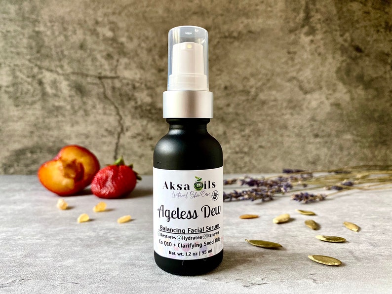 Może przedstawiać: Czarna szklana butelka z srebrną pompką i białą etykietą z napisem "Aksa Oils Natural Skin Care Ageless Dew Balancing Facial Serum Restores Hydrates Renews Co Q10 Clarifying Seed Oils Net Wt. 1.2 oz | 35 ml"