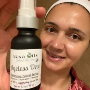 Może przedstawiać: Czarna butelka z białą pompką i etykietą z napisem "Aksa Oils Natural Skin Care Ageless Dew Balancing Facial Serum Nature's Hydrating Balance 100% Clarifying Seed Oil Net Wt. 1.7 oz / 50 ml"