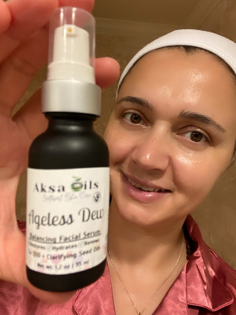 Może przedstawiać: Czarna butelka z białą pompką i etykietą z napisem "Aksa Oils Natural Skin Care Ageless Dew Balancing Facial Serum Nature's Hydrating Balance 100% Clarifying Seed Oil Net Wt. 1.7 oz / 50 ml"