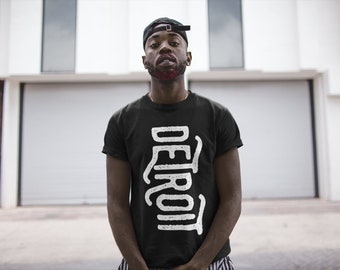 Könnte beinhalten: Ein schwarzes T-Shirt mit einem weißen Grafikdruck des Wortes "DETROIT" in einer stilisierten Schrift.