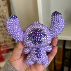 May include: A purple and blue rhinestone Stitch figurine with a large, sparkly, purple eye.