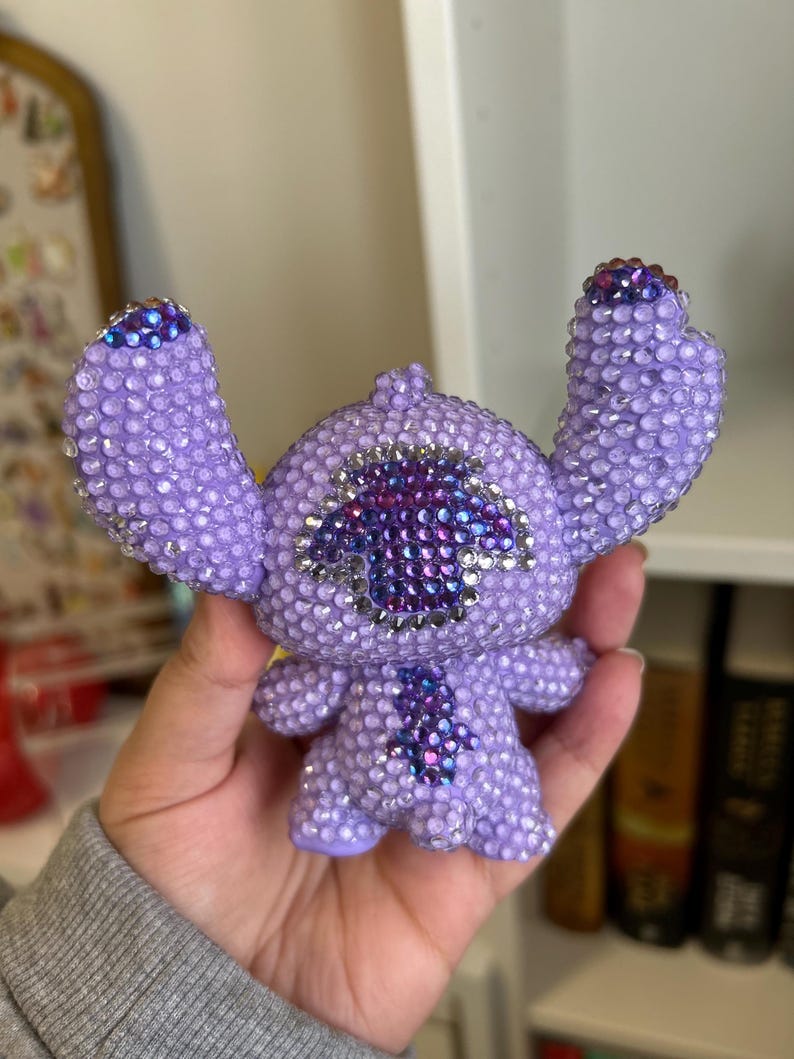 May include: A purple and blue rhinestone Stitch figurine with a large, sparkly, purple eye.