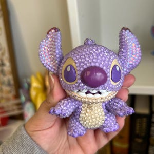May include: Purple and white rhinestone Stitch figurine with a toothy grin.