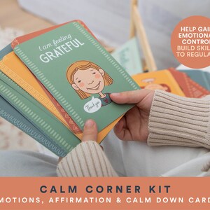 K&ouml;nnte beinhalten: Ein Satz bunter Karten mit Illustrationen und Text. Die Karten sind mit "Calm Corner Kit" und "Emotions, Affirmation & Calm Down Cards" beschriftet. Eine Karte lautet "Ich bin dankbar" und zeigt ein Cartoon-M&auml;dchen mit einem gl&uuml;cklichen Gesichtsausdruck. Der Text "Hilft, emotionale Kontrolle zu gewinnen, F&auml;higkeiten zum Regulieren aufzubauen" ist im Hintergrund sichtbar.